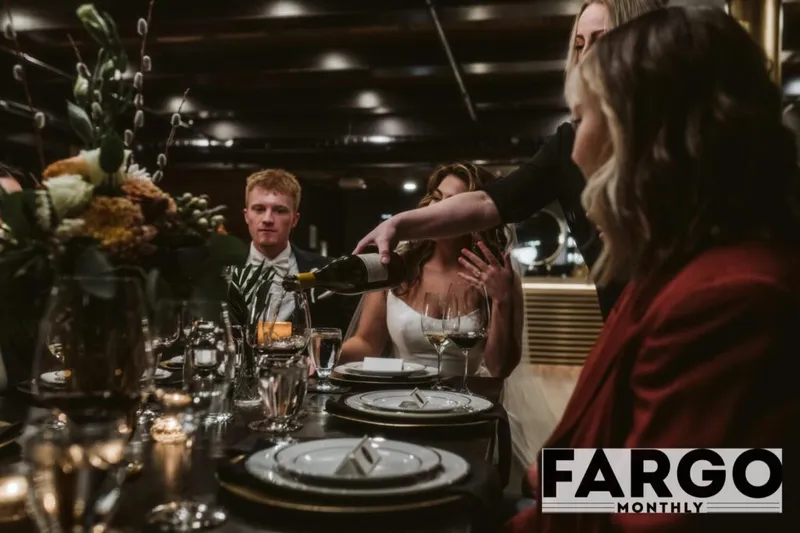 Server pouring wine at an elegantly set dinner table with floral centerpiece and candlelight