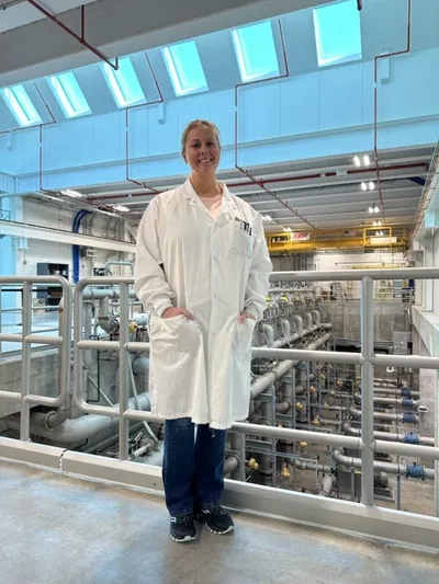 Woman in white lab coat standing on a mezzanine overlooking industrial water treatment equipment