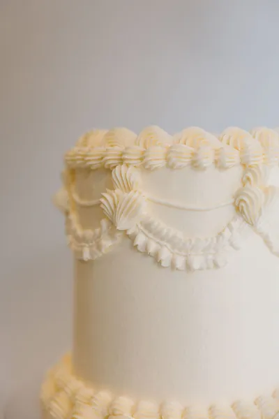 Close-up of a white tiered cake with intricate piped frosting swags and scalloped edges