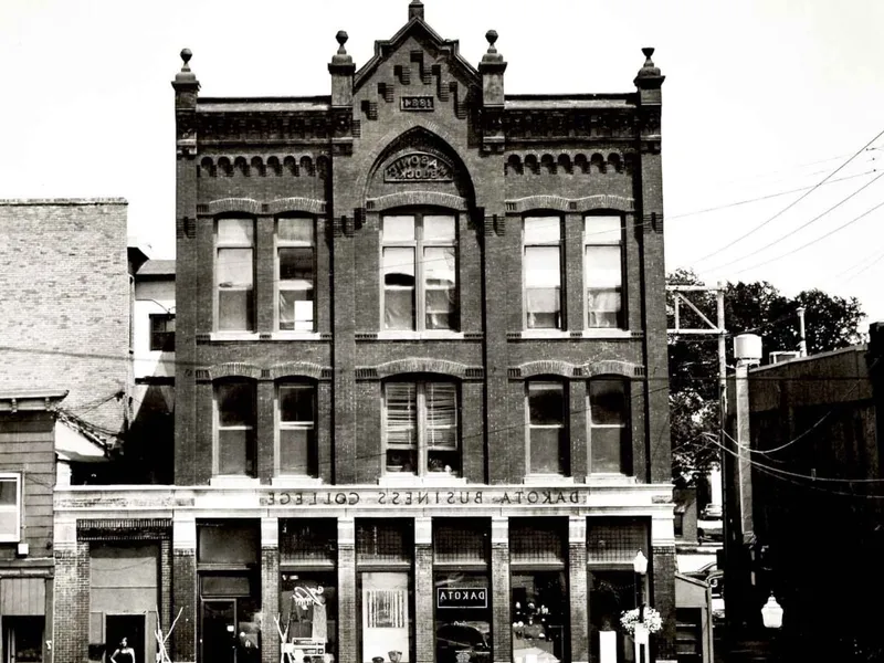 Black-and-white photo of a two-story brick building with ornate Gothic facade reading Dakota Business College