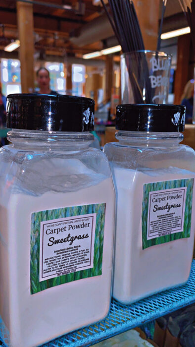 Two jars of Sweetgrass Carpet Powder with black lids on a blue wire shelf