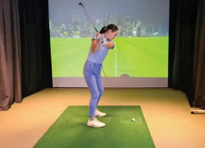 Woman mid-swing with a golf club at an indoor simulator bay