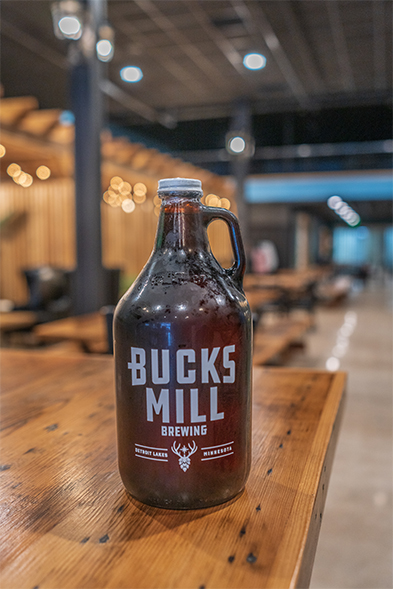 Bucks Mill Brewing amber glass growler on a wood bar top in a modern taproom