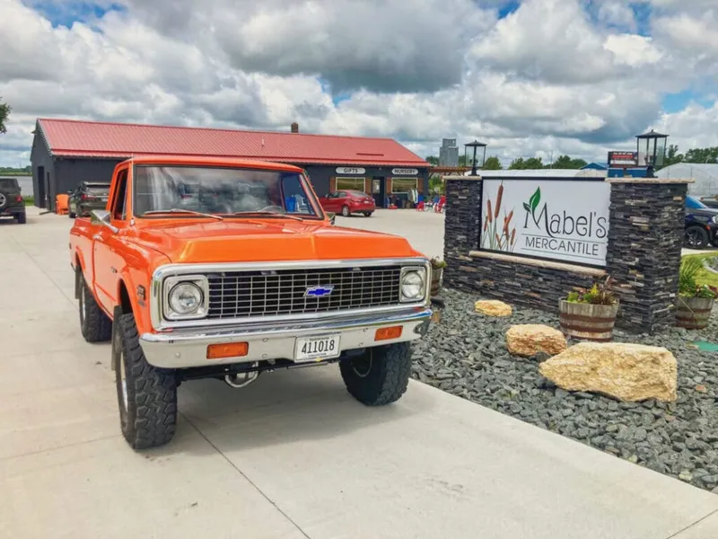 Vintage orange Chevrolet pickup truck parked outside Mabel's Mercantile under a cloudy sky