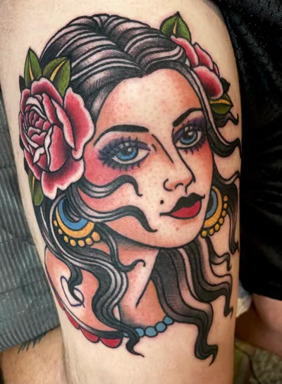 Traditional-style tattoo of a woman's face with roses and hoop earrings on an arm