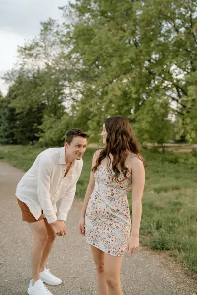 Man in white shirt leaning toward smiling woman in floral dress on a park path