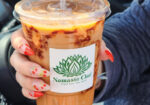 Hands holding an iced drink in a clear cup with a branded sleeve