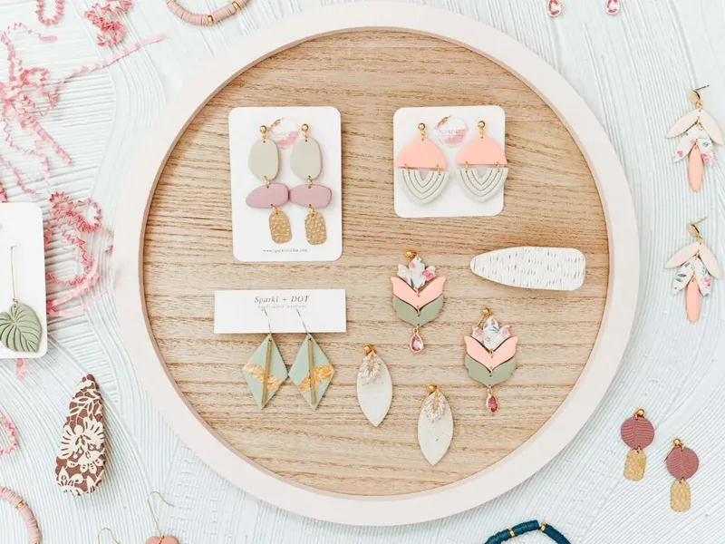 Handmade earrings in pastel pink, sage, and gold displayed on a round wooden tray