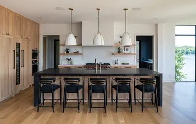 Modern kitchen with dark island, black barstools, and pendant lights overlooking a lake
