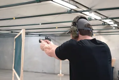 Man in black shirt and ear protection aiming a handgun at an indoor shooting range