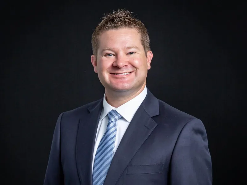 Smiling man in navy suit and blue striped tie against dark background