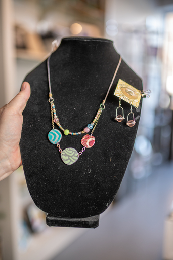 Colorful beaded necklace and small drop earrings displayed on a black jewelry bust