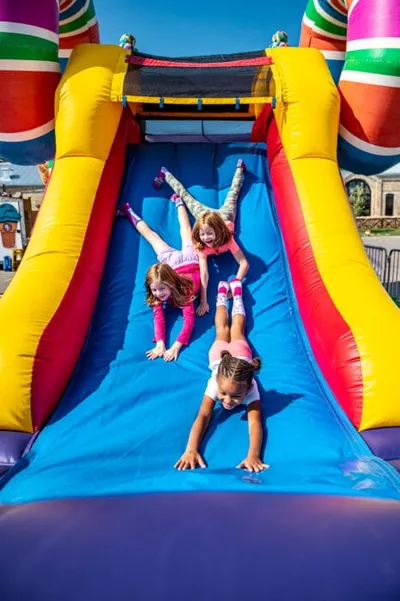 Three girls sliding down a colorful inflatable bounce house slide outdoors