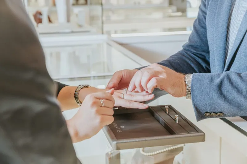 Jeweler placing a ring on a customer's finger over a display tray at a jewelry counter