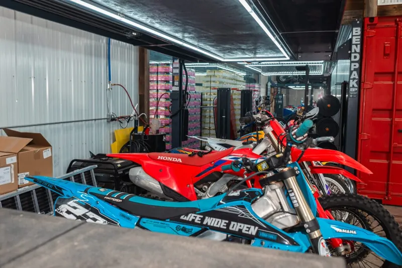 Red Honda and blue dirt bike parked inside a well-lit garage workshop