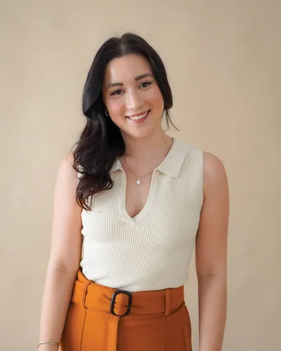 Smiling young woman in cream ribbed polo top and rust-orange belted trousers