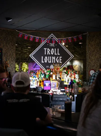Interior of the Troll Lounge bar with a diamond-shaped sign, Norwegian flags, and shelves of bottles