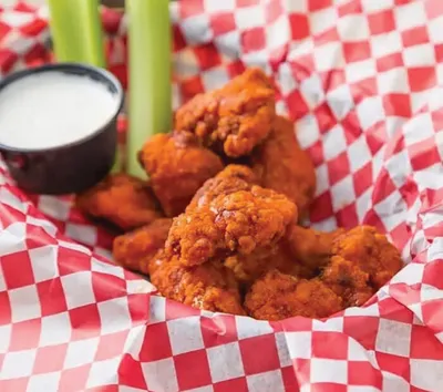 Saucy fried chicken wings in a red-checkered basket with celery sticks and a dipping sauce