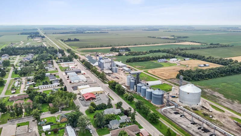 Aerial view of a small rural town with grain silos, tree-lined streets, and vast cropfields beyond