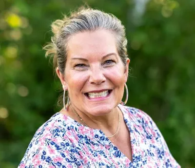 Smiling woman with blond-gray hair wearing a floral top outdoors