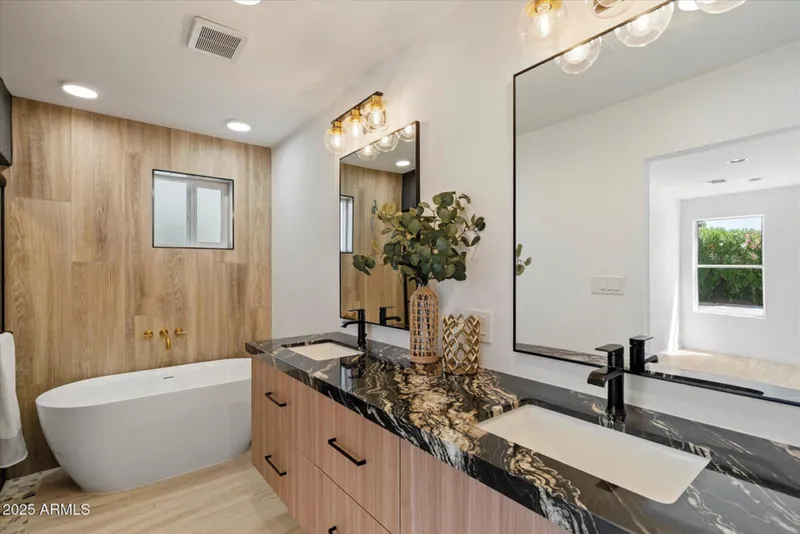 Modern bathroom with dark marble double vanity, wood-panel accent wall, and freestanding soaking tub