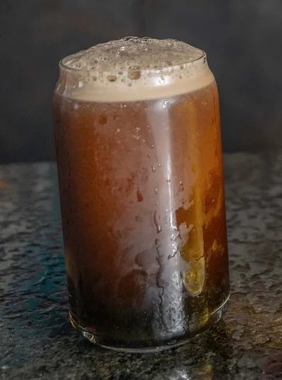 Condensation-covered pint glass of dark beer with a frothy head on a stone surface