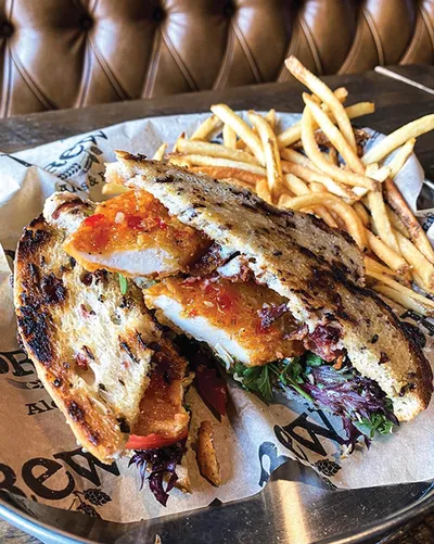 Grilled panini halves with chicken and jam on toasted bread, served with thin-cut fries on a metal tray