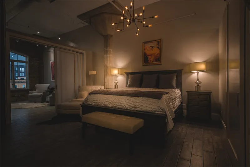 Dimly lit bedroom with dark wood floors, a sputnik chandelier, and a king bed flanked by table lamps