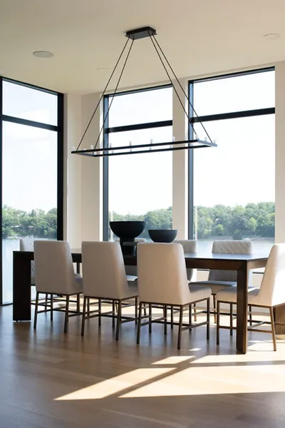 Modern dining room with dark wood table, upholstered chairs, and floor-to-ceiling windows overlooking a lake
