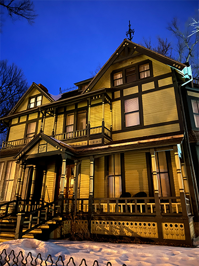 Victorian house lit up at night with snow on the ground under a deep blue winter sky