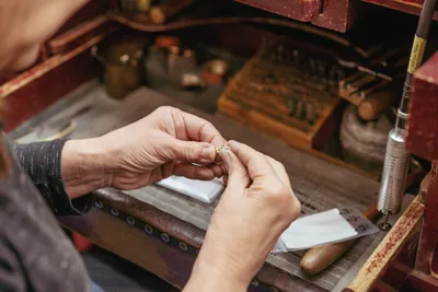 Jeweler's hands carefully working on a small ring at a cluttered workbench