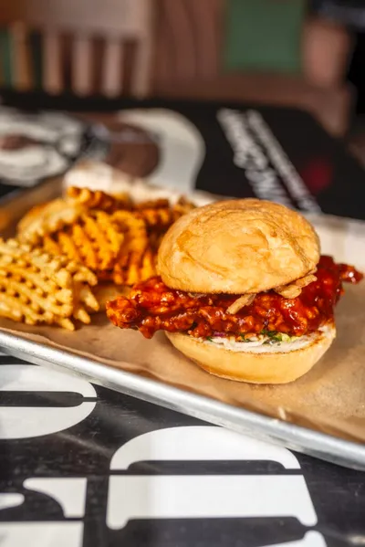 Saucy fried chicken sandwich with waffle fries on a parchment-lined metal tray