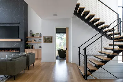 Modern open-plan living area with black marble fireplace, floating wood stairs, and cable railing