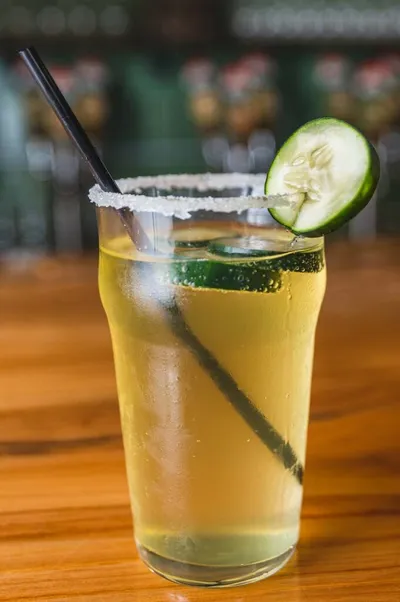 Chilled cocktail with salted rim, cucumber slices, and black straw on a wood bar