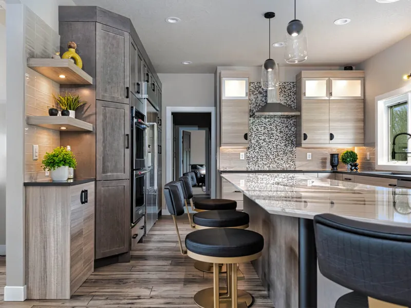 Modern kitchen with gray wood cabinets, black-and-gold bar stools at a marble island, and mosaic tile backsplash