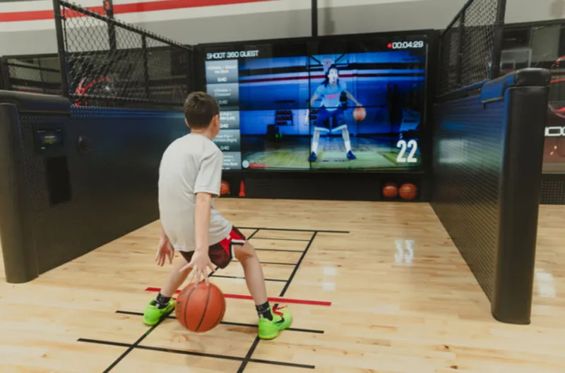 Young boy dribbling a basketball in front of a large interactive training screen