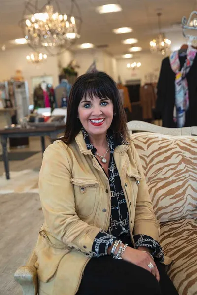 Smiling woman in a yellow jacket seated on a zebra-print sofa inside a boutique