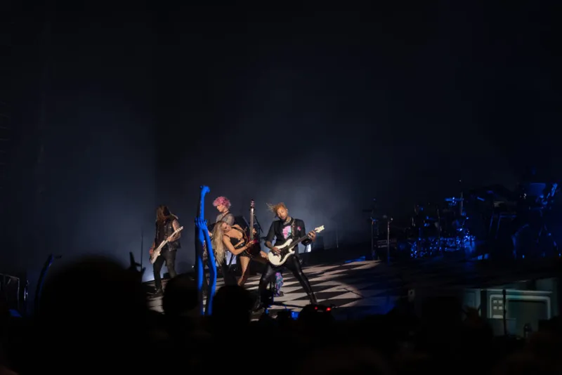 Rock band performing on a darkened stage with dramatic spotlight and hazy atmosphere