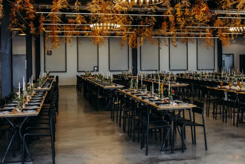 Banquet hall with long wooden tables, black chairs, tapered candles, and amber dried botanicals hanging from the ceiling