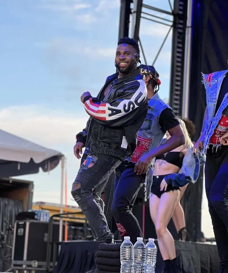 Smiling male performer in a USA jacket and ripped jeans dancing on an outdoor stage