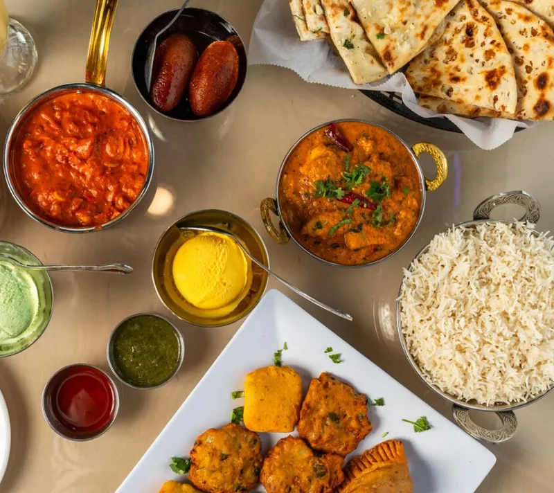 Overhead spread of Indian dishes including curry, basmati rice, naan, chutneys, and fried appetizers