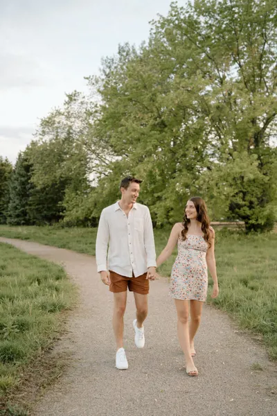 Couple holding hands and smiling at each other while walking a park path
