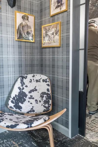 Cow-print chair against grey plaid wallpaper with gold-framed artwork above