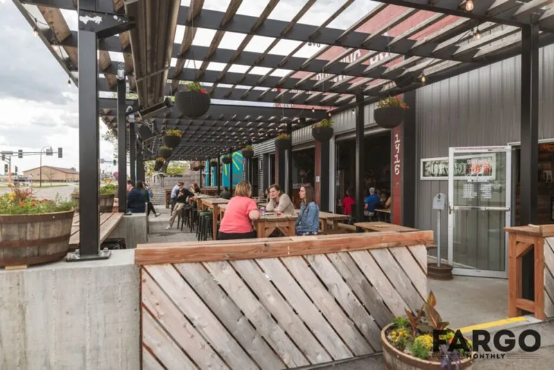 Outdoor restaurant patio with pergola, wood-plank divider, and diners seated at picnic tables