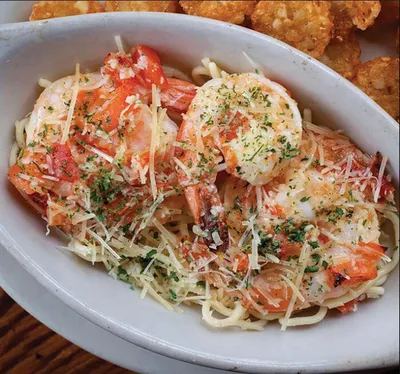 Shrimp pasta in a white oval dish topped with shredded parmesan and fresh herbs