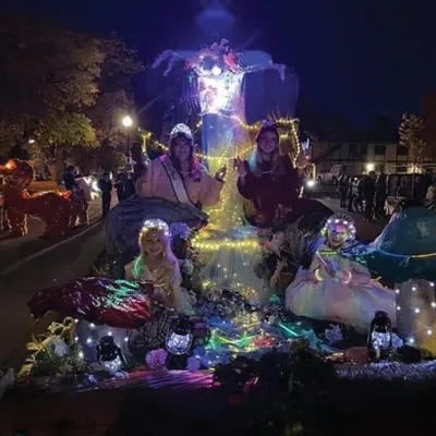 Illuminated night parade float with costumed performers surrounded by colorful string lights