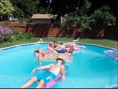 Group of people relaxing on colorful pool floats in a backyard swimming pool