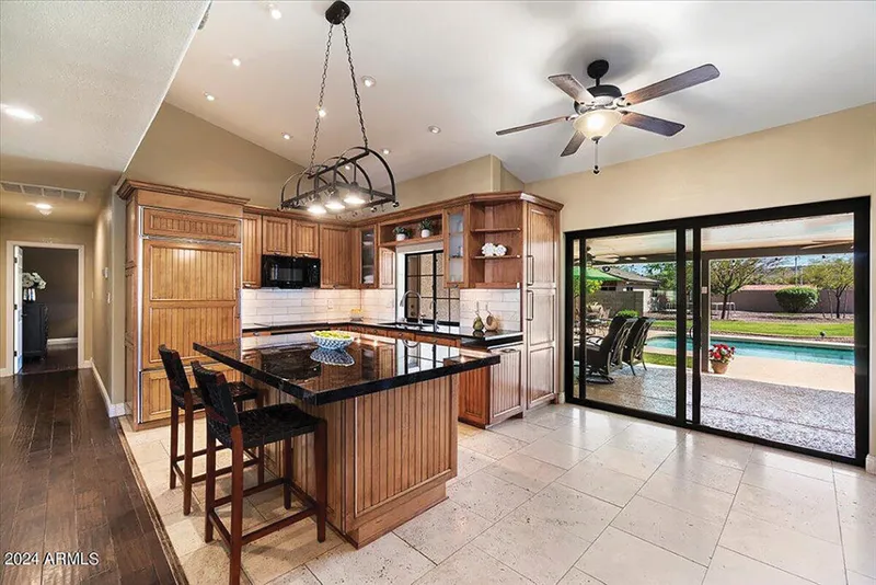 Kitchen with wood cabinetry, black granite island, and sliding doors opening to a backyard pool