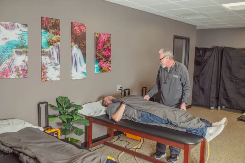 Practitioner standing beside a patient lying on a treatment table wrapped in a gray blanket