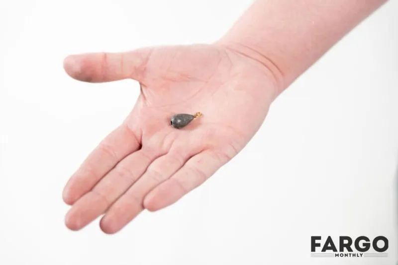 Open palm holding a small teardrop-shaped fishing sinker with a gold swivel